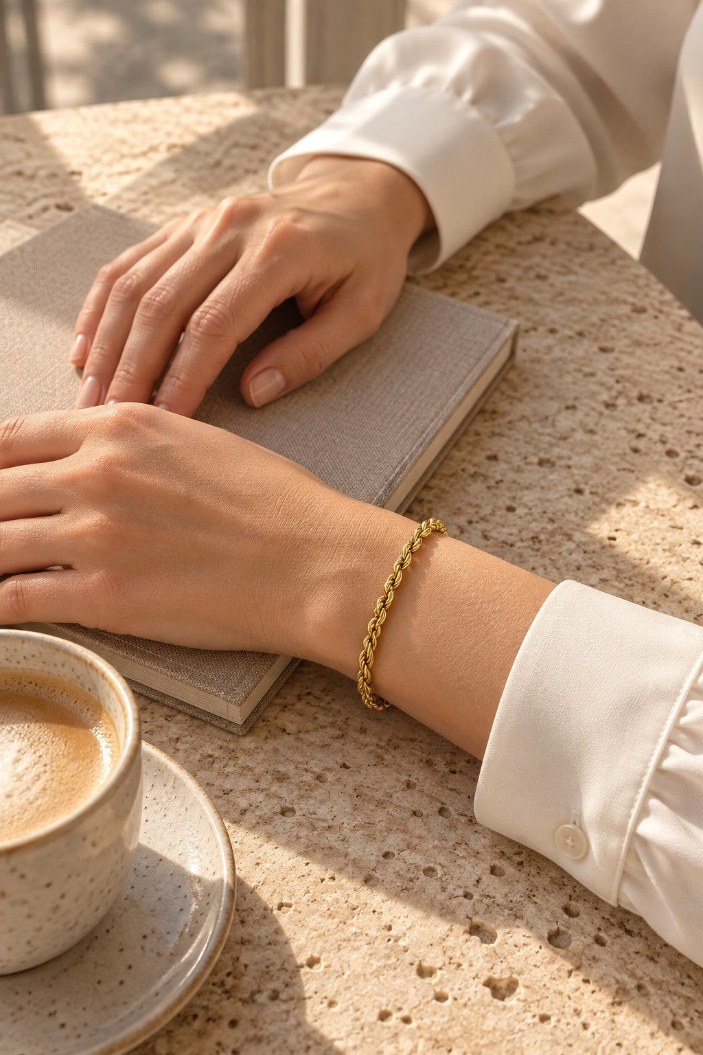 Editorial close-up of a gold-tone rope bracelet on a sleeved wrist